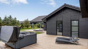 En modern uteplats med ett bubbelbad, solstolar och en grillplats under tak.