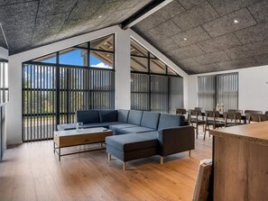 A modern interior with a sectional sofa, wooden flooring, and large windows. - 4 Star Holiday Home in Lokken (Lokken)