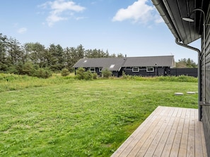 A black building with a sloped roof, surrounded by a grassy area and trees. - 4 Star Holiday Home in Lokken (Lokken)