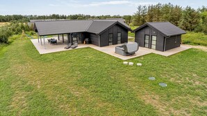 Ett modernt hus i två våningar med en uteplats, utomhusmöbler och en stor utomhusvärmare.