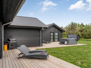 Una terrassa amb una barbacoa, seients i una banyera d'hidromassatge.