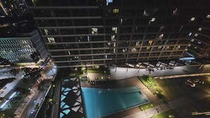 A nighttime view of a high-rise building with a swimming pool, a covered area, and a street with cars. - Casa Rogelio at Fame Residences Tower 4 (Mandaluyong)