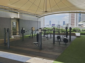 An outdoor gym with various exercise equipment, a covered area, and a cityscape view in the background. - Casa Rogelio at Fame Residences Tower 4 (Mandaluyong)