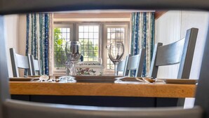 Une table à manger avec des chaises, une nappe à motifs floraux et une vue sur une fenêtre avec des rideaux.