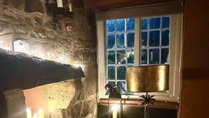 Une cheminée en pierre avec des bougies, une fenêtre donnant sur un beau paysage et un canapé vert.