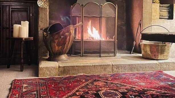 Une cheminée en pierre avec un feu de bois, un banc en bois rustique et un tapis à motifs.