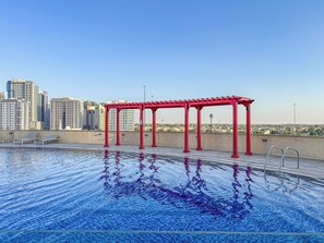 Piscina en la azotea con una pérgola roja y el horizonte de la ciudad al fondo.