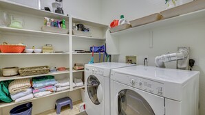 A laundry room with two front-loading washing machines, shelves with laundry supplies, and a small stool. - On Johnson Ranch Golf Course: San Tan Valley Home (San Tan Valley)