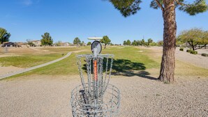 A disc golf basket with a metal cage and chains, surrounded by a gravel area with a path leading to houses in the background. - On Johnson Ranch Golf Course: San Tan Valley Home (San Tan Valley)