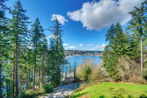 Uma área arborizada com uma estrada que leva a um corpo d'água, provavelmente um lago, e vista para uma cidade distante.