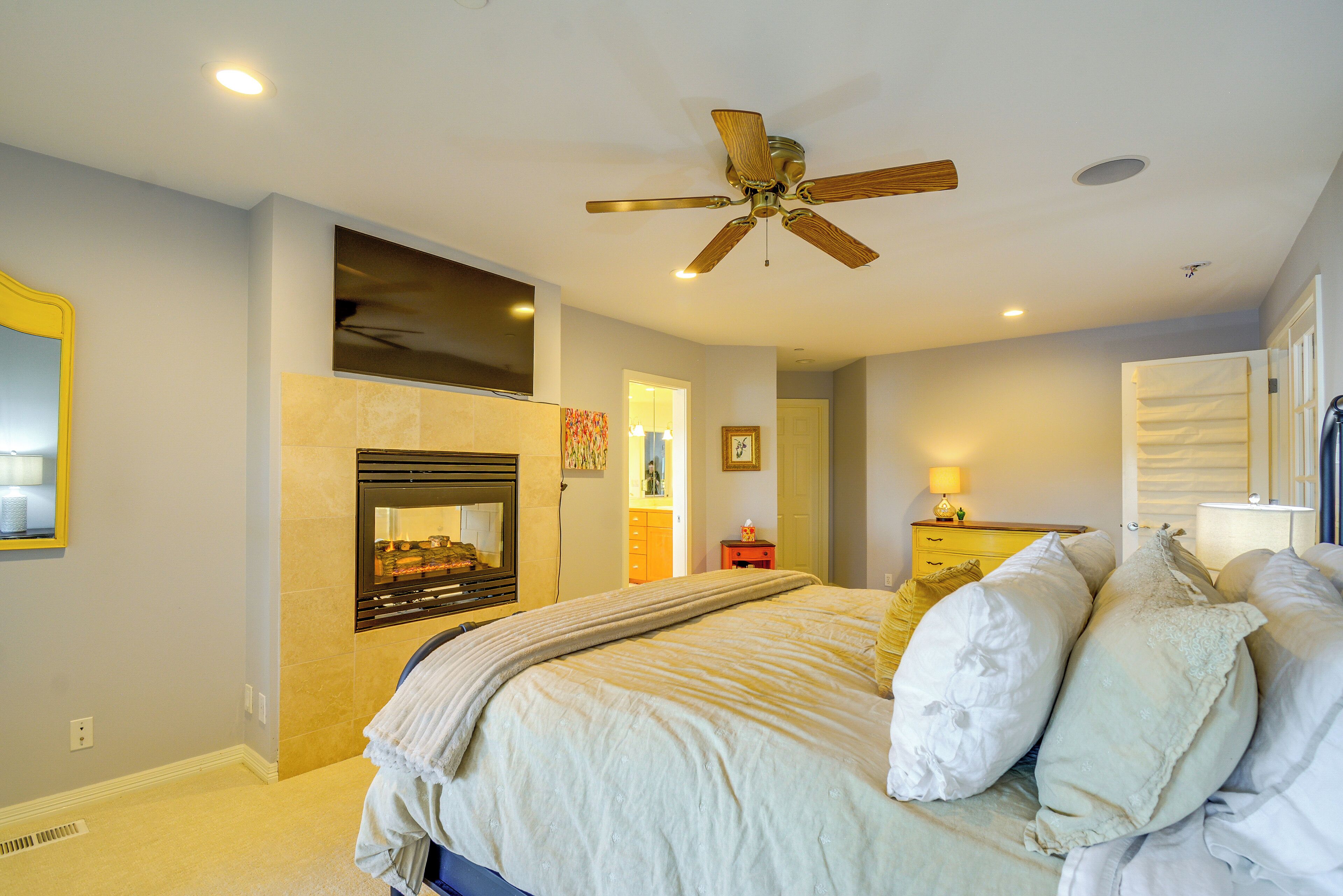 A bedroom with a bed, a ceiling fan, a fireplace, and a nightstand with a lamp.