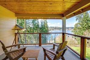 A wooden deck with two Adirondack chairs and a small table, overlooking a lake and forested area. - Premier Gig Harbor Home! Views, Spa & Billiards (Gig Harbor)