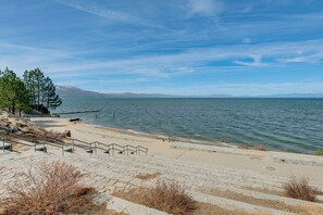 Eine Steintreppe führt zu einem Strand mit Blick auf das Wasser und ferne Berge.