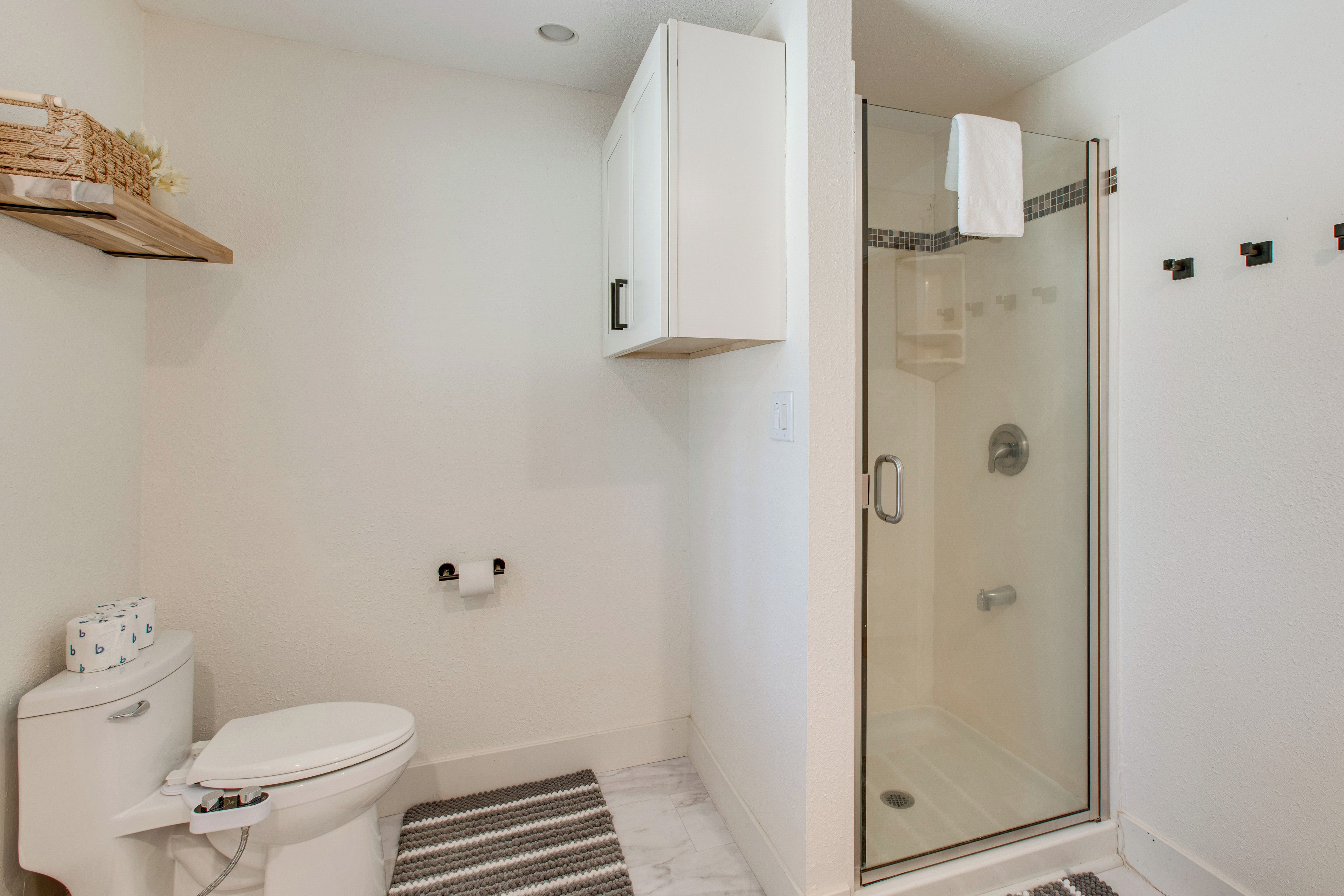 A bathroom with a toilet, a glass shower enclosure, and a white cabinet.