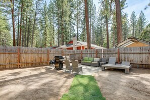 Ein Garten mit Holzzaun, Gartenmöbeln, einem Grill und einem überdachten Bereich.