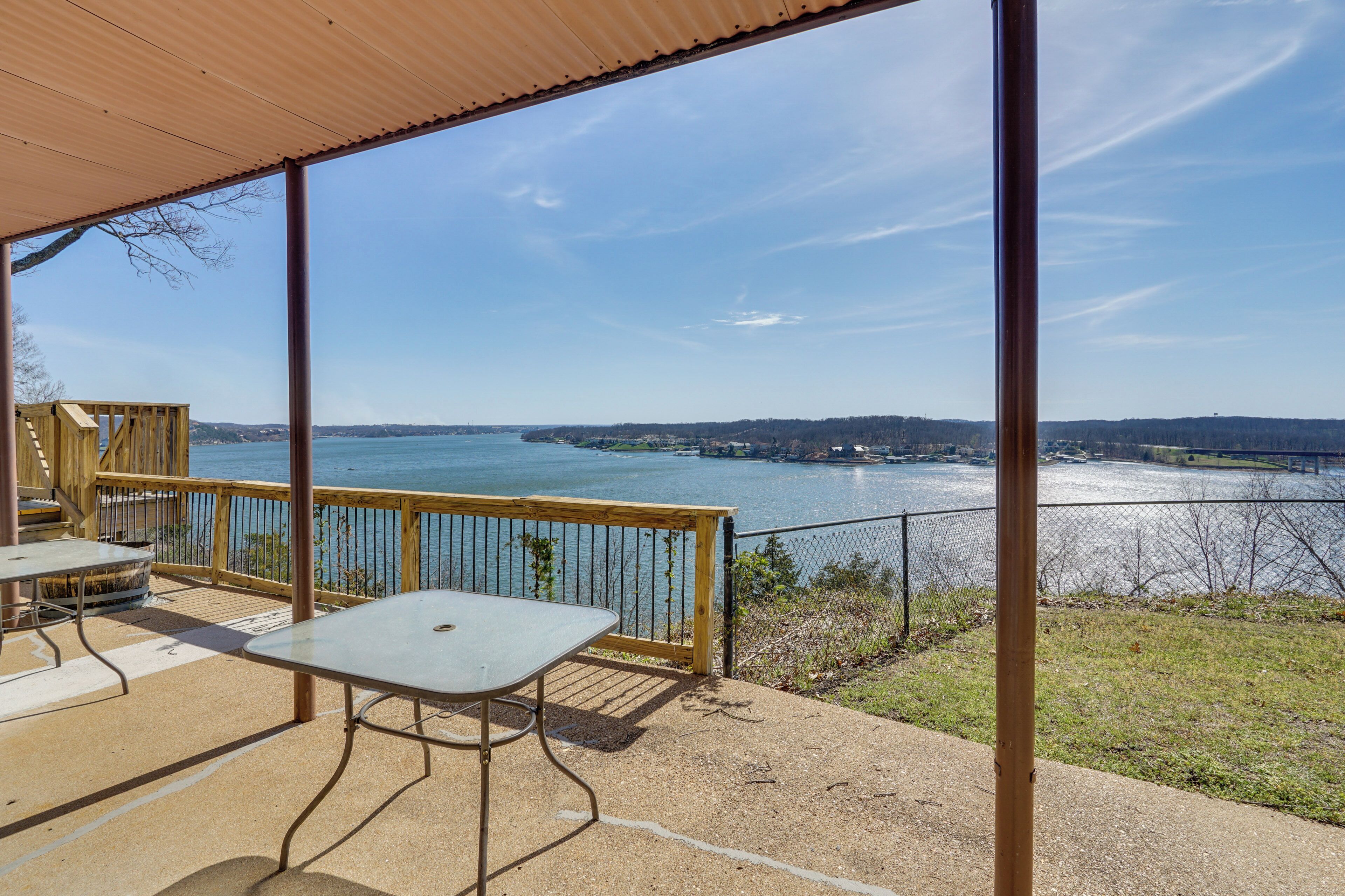 A covered outdoor area with a table and chairs, overlooking a body of water and distant land.