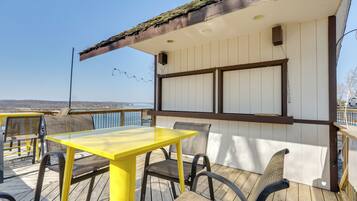 A deck with a yellow table and chairs, a white wall with a window, and a view of the landscape.
