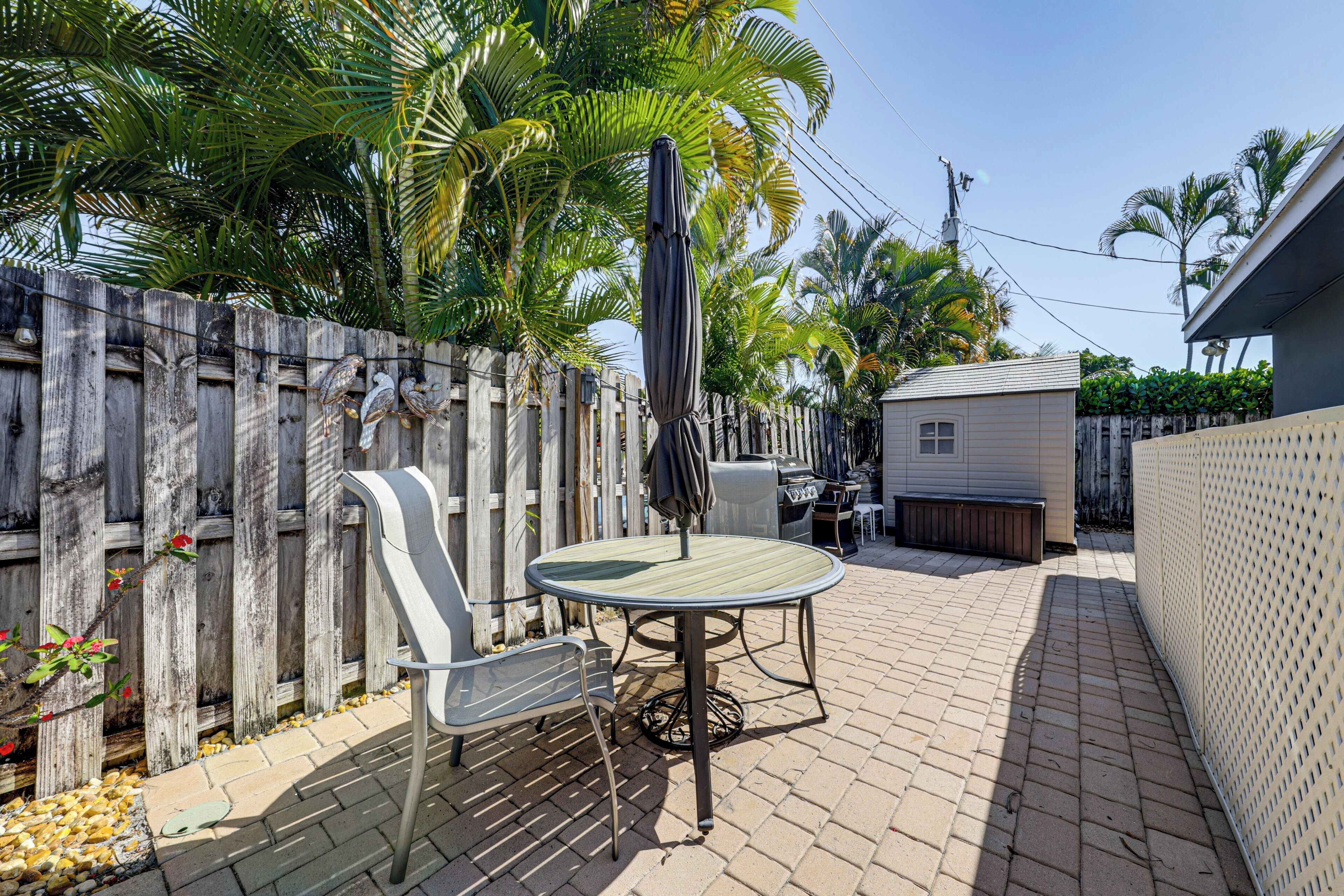 A patio with a table and chairs, a grill, and a wooden fence.
