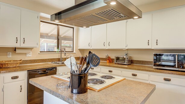 A modern kitchen with white cabinets, a stainless steel range hood, a built-in oven, and a microwave. - Creative Escape! Eagle's Nest Hideaway (Cottage Grove)