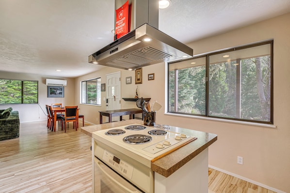 A modern kitchen with a central island, a dining area with a table and chairs, and large windows with a forest view.