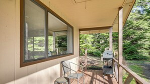 A covered porch with a view of a wooded area, a grill, and a chair. - Creative Escape! Eagle's Nest Hideaway (Cottage Grove)