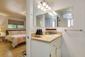 A bathroom with a sink, mirror, towel rack, and a bed in the adjacent room. - Creative Escape! Eagle's Nest Hideaway (Cottage Grove)