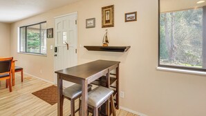 A room with a wooden table, two chairs, a window with a view of trees, a door, and wall-mounted pictures. - Creative Escape! Eagle's Nest Hideaway (Cottage Grove)