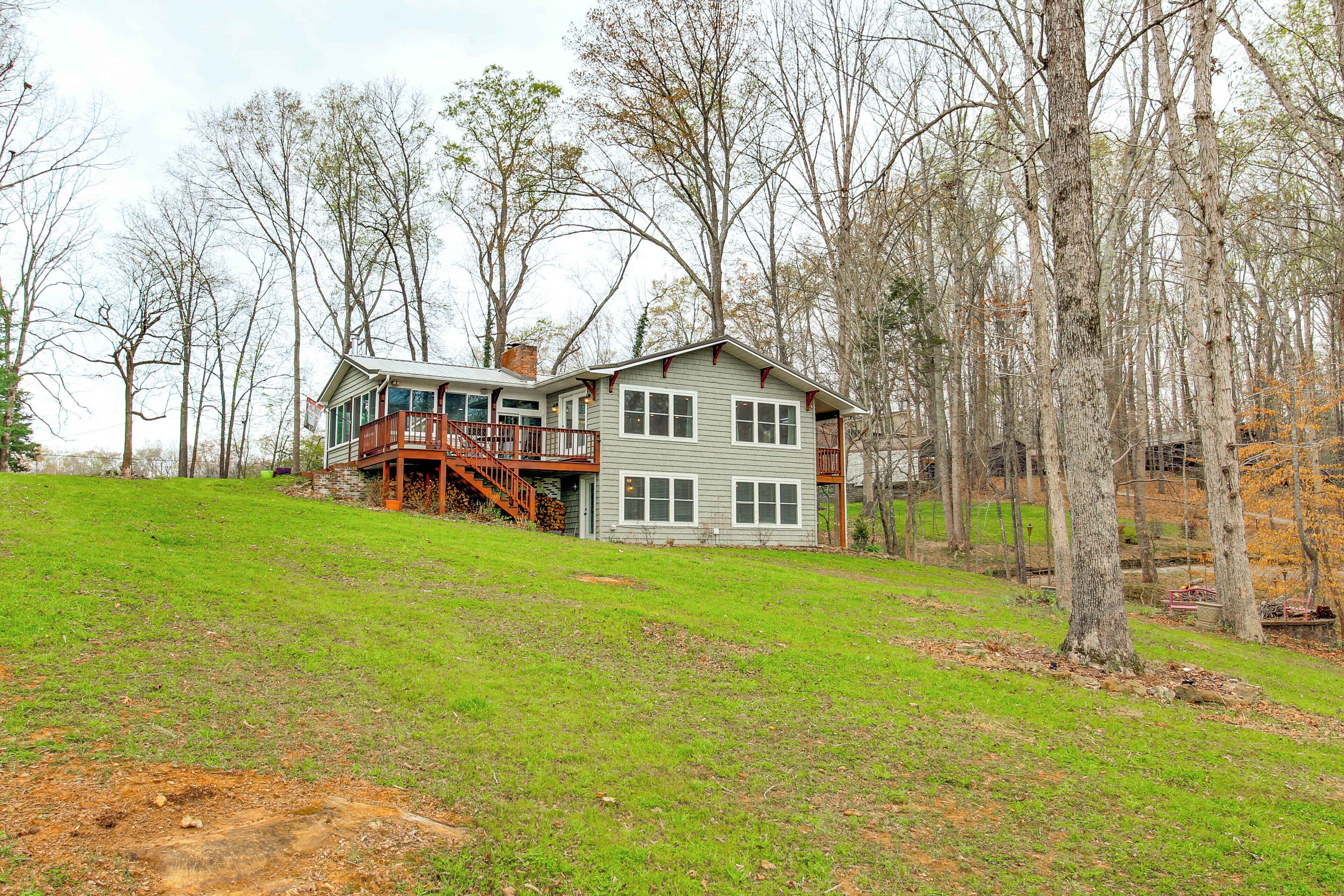 A two-story house with a deck, surrounded by trees and a grassy area.