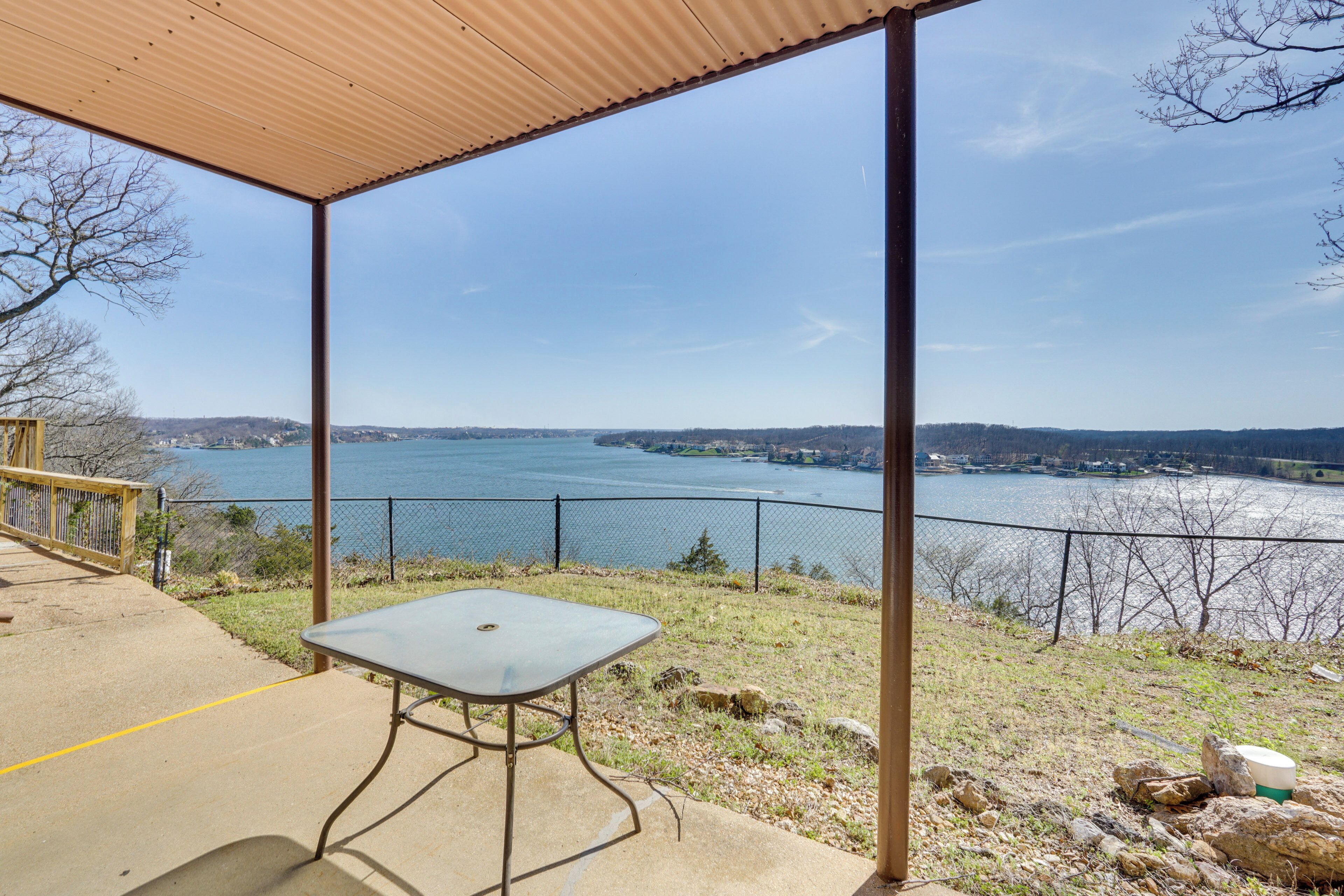 A covered outdoor area with a table, overlooking a body of water and distant land.