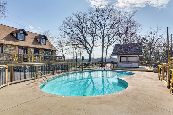 A swimming pool with a curved design, a covered deck area, and a building with a sloped roof in the background. - Unit 3: Main Channel View! Studio By Bagnell Dam (Lake Ozark)