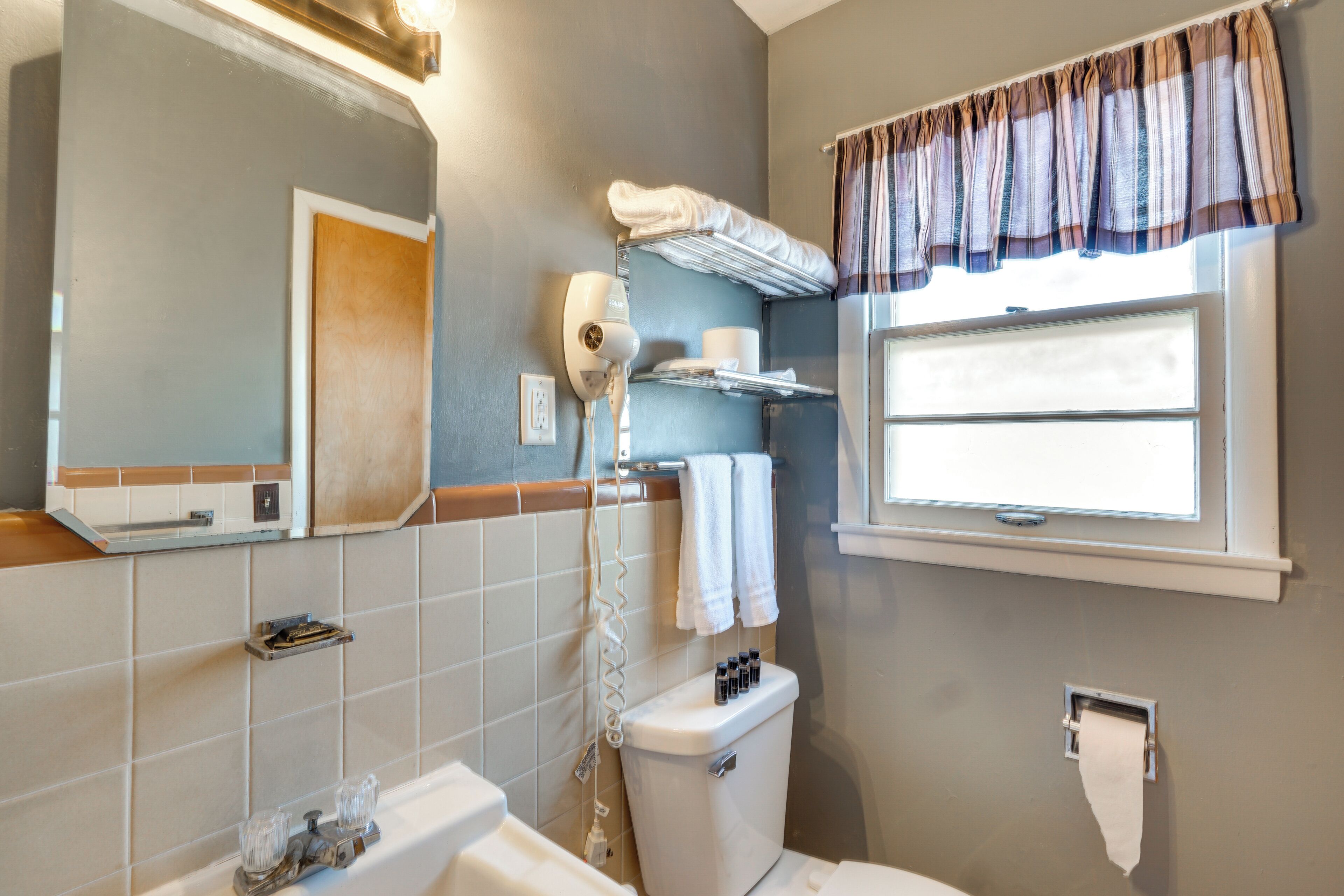 A bathroom with a toilet, a sink, a mirror, a towel rack, and a window with curtains.
