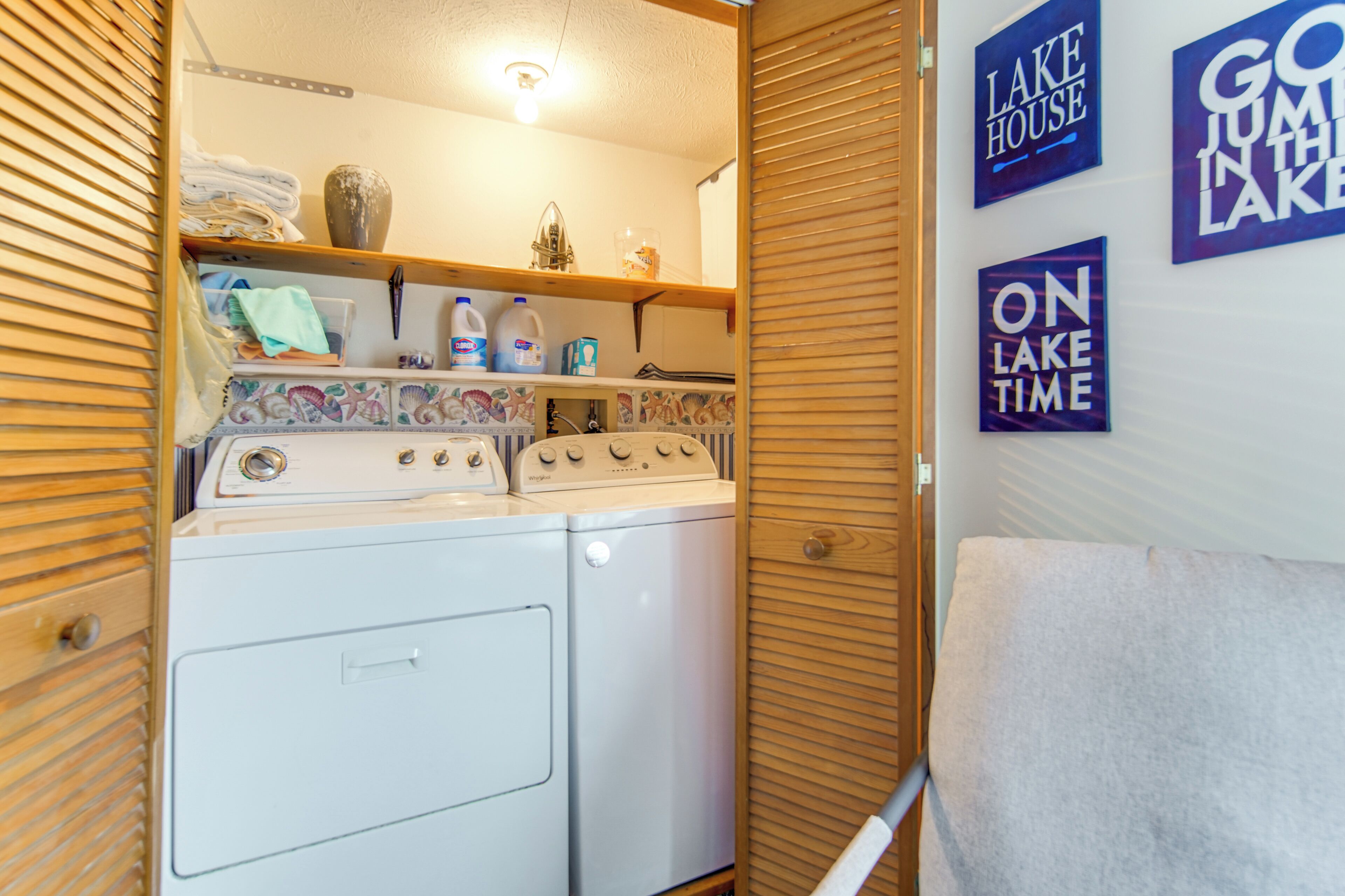 A laundry room with a washing machine, dryer, and shelves with folded clothes and bottles.