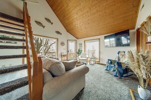 Amplia sala de estar con una escalera de madera, un sofá, una mesa de centro y un gran ventanal.