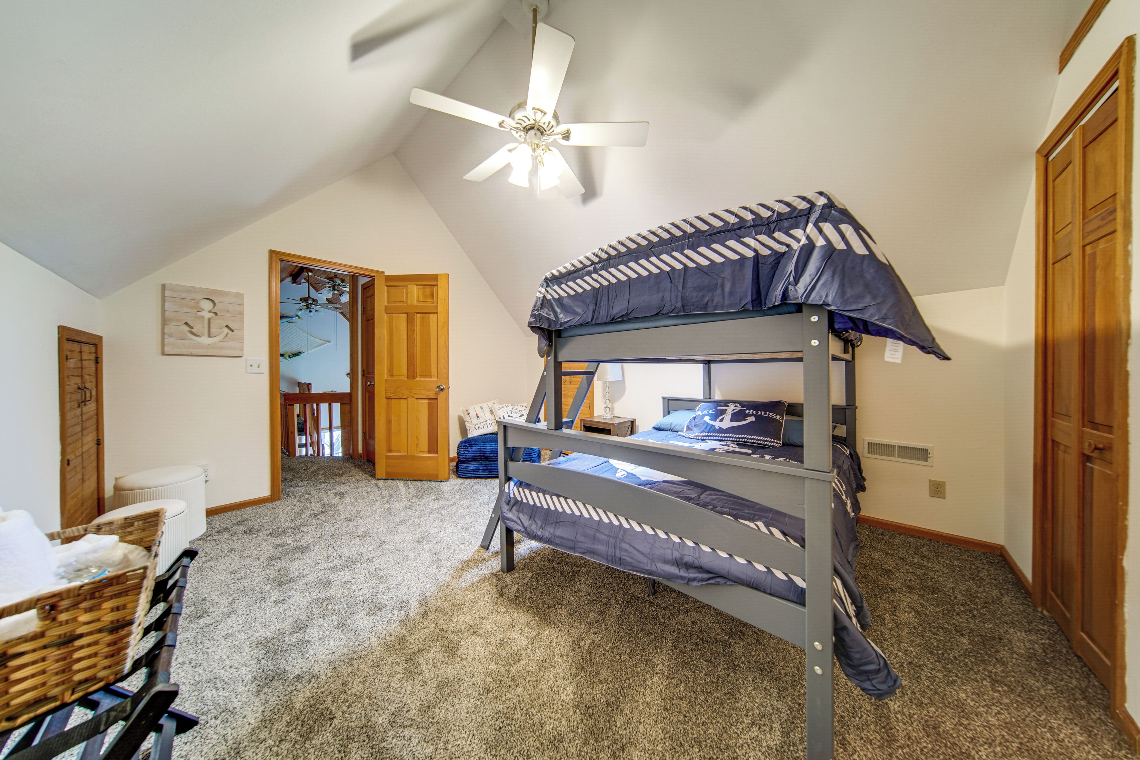 A bunk bed room with a ceiling fan, a door leading to another room, and a carpeted floor.