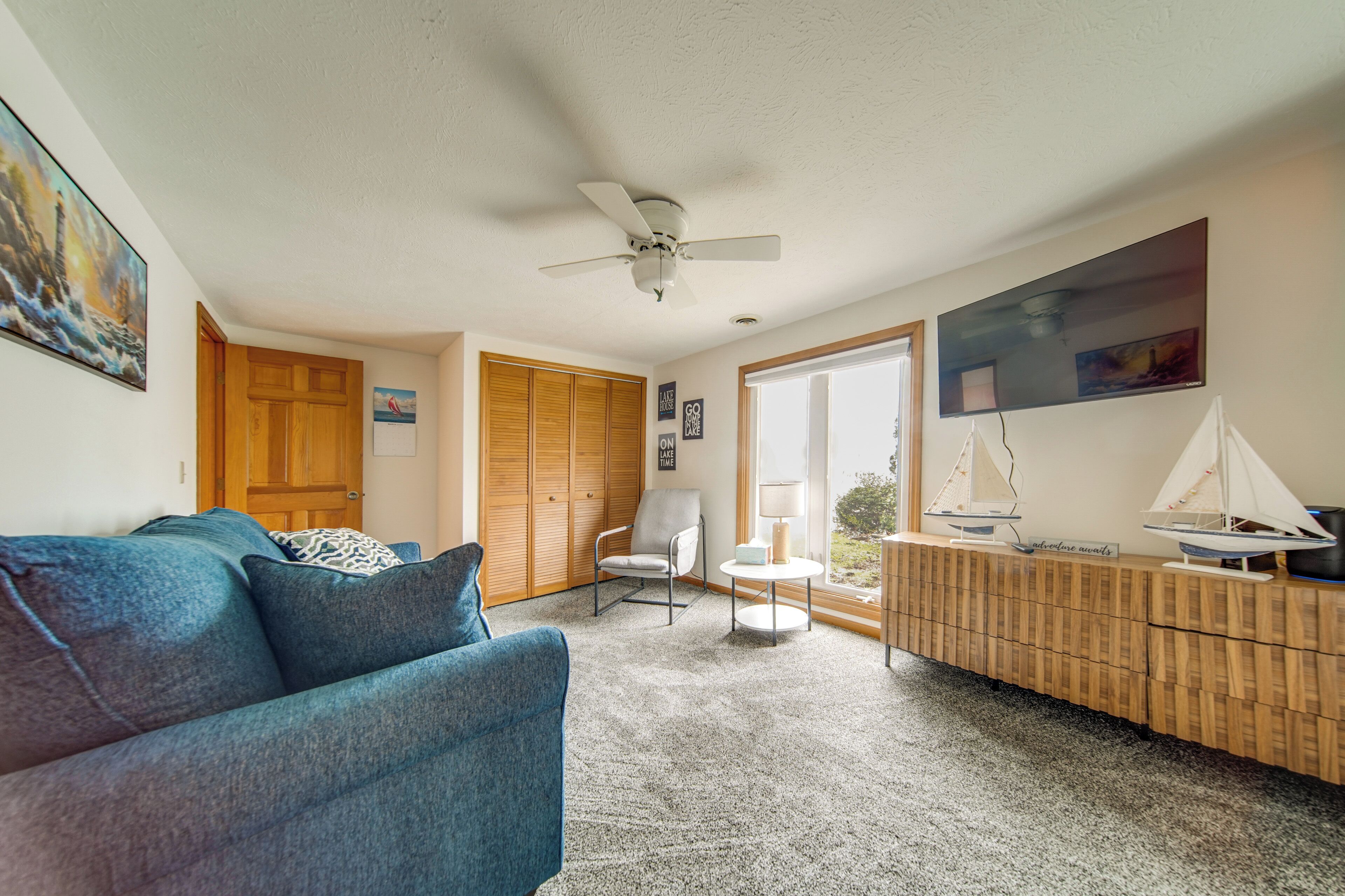 Ein Wohnzimmer mit einem blauen Sofa, einem Deckenventilator, einem Holzschrank und einem Fenster mit Ausblick.