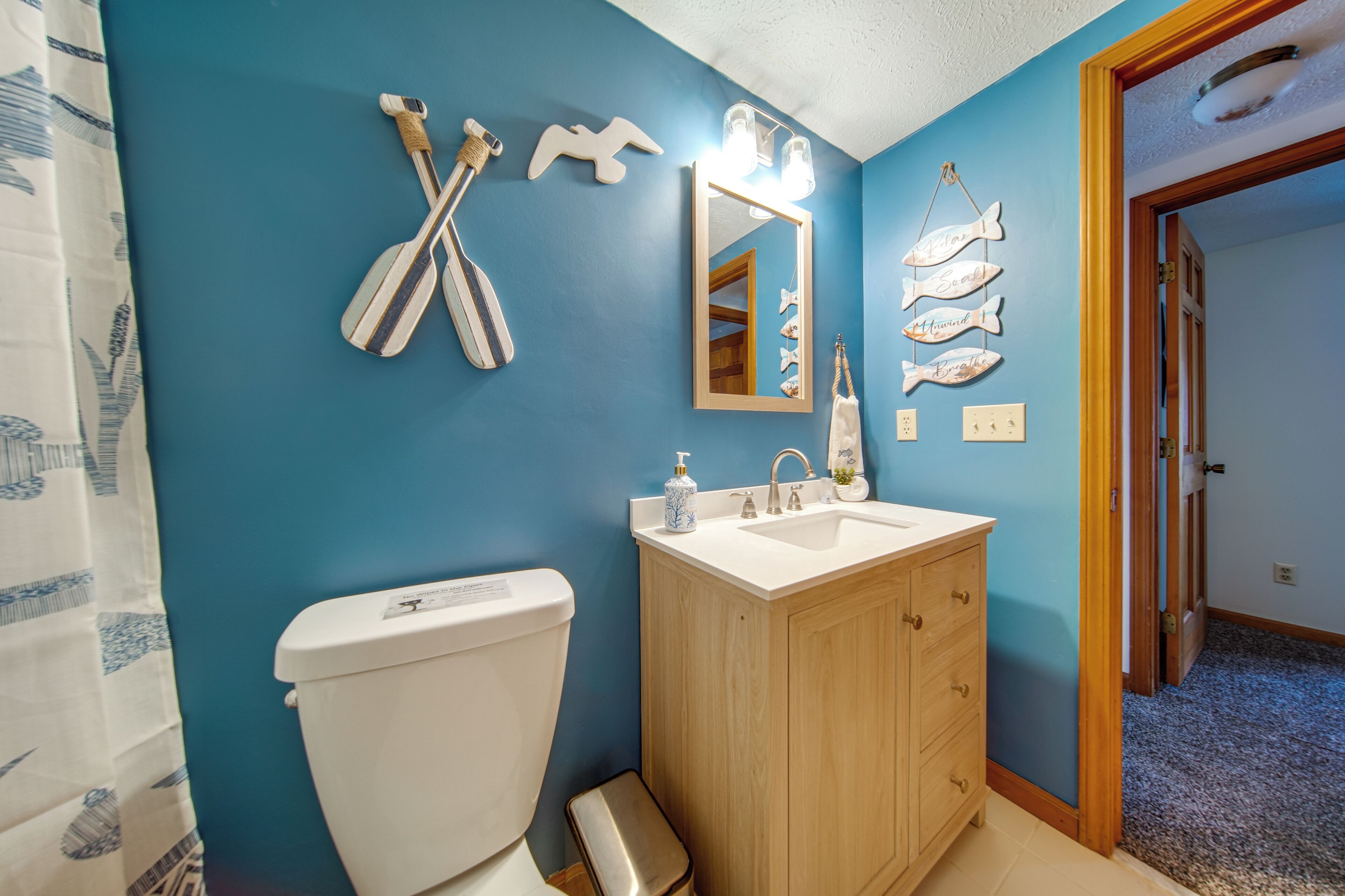 A bathroom with a blue wall, wooden vanity, white toilet, and decorative fish wall art.