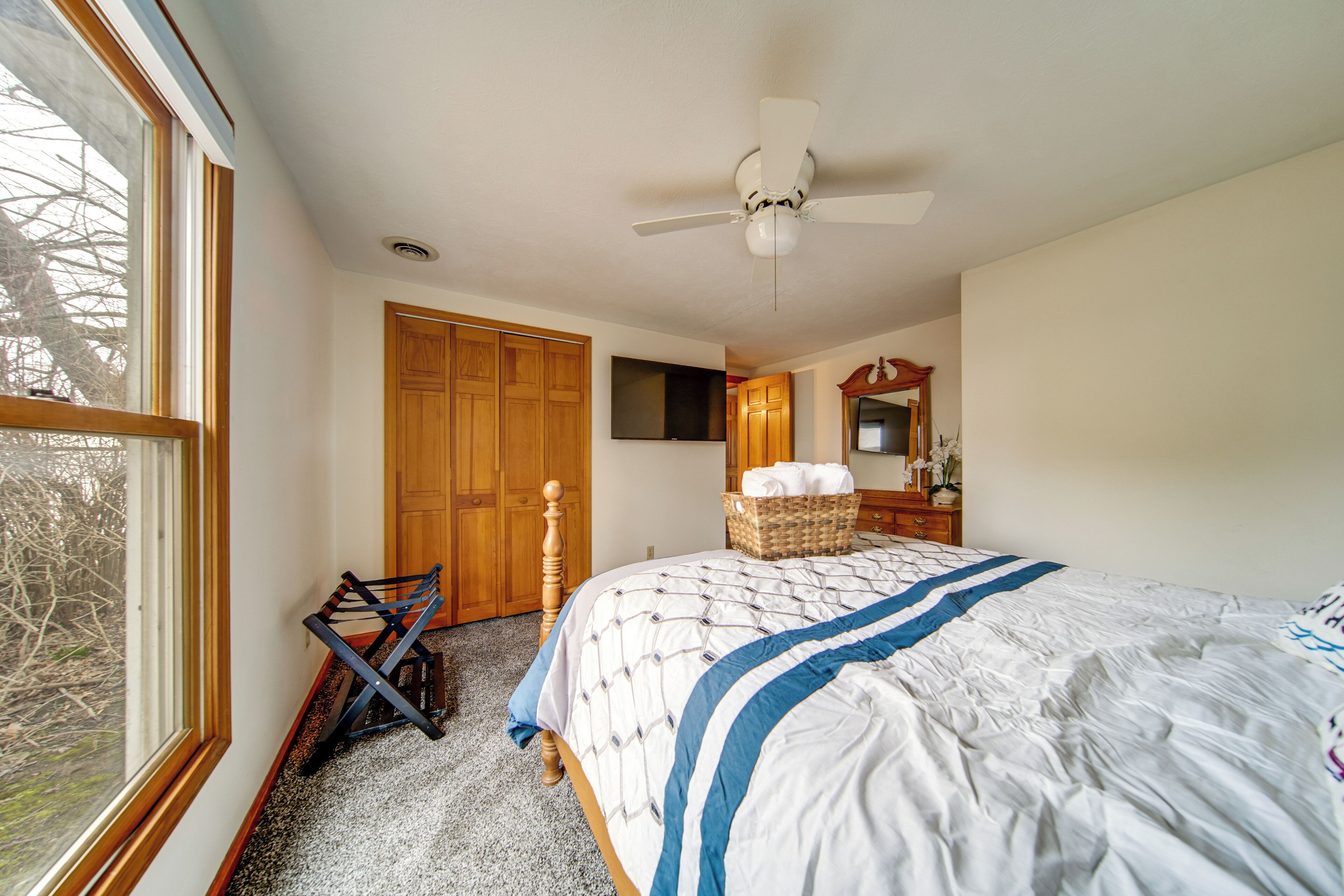Un dormitorio con cama, ventilador de techo, armario de madera, televisor y ventana.