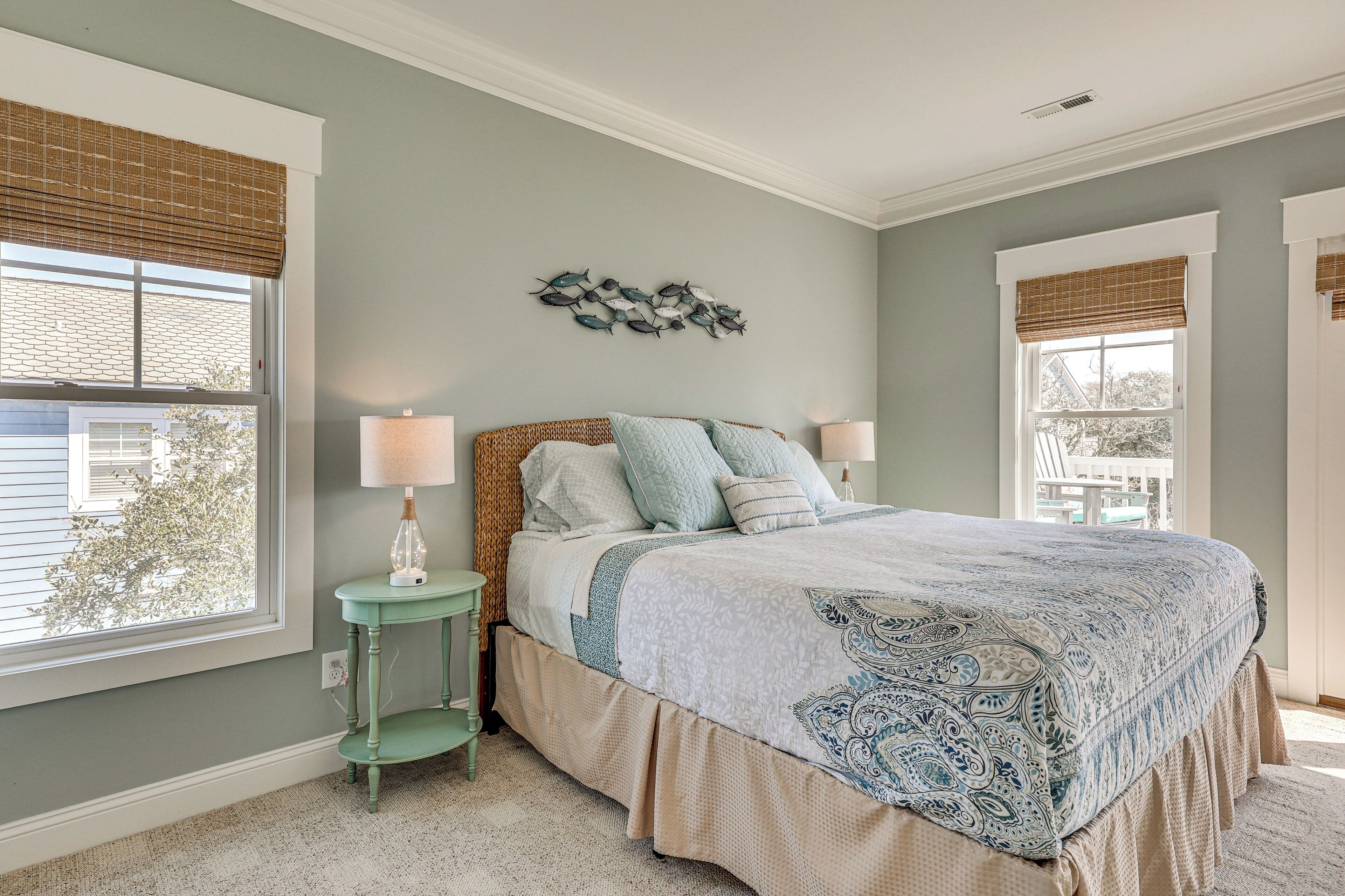A bedroom with a bed, two bedside tables, a wall decoration, and large windows.