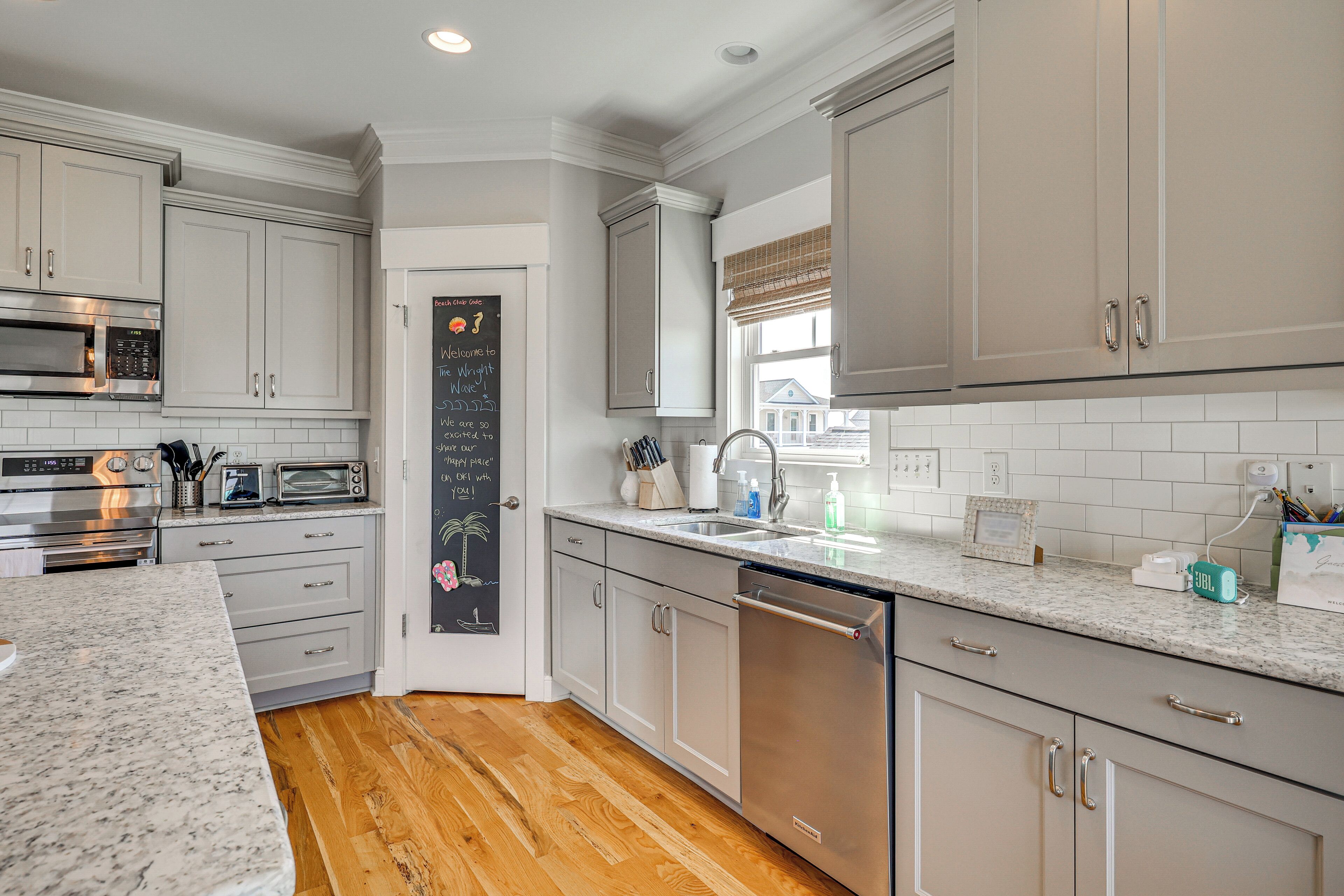 A modern kitchen with white cabinets, a granite countertop, stainless steel appliances, and a chalkboard with a welcome message.