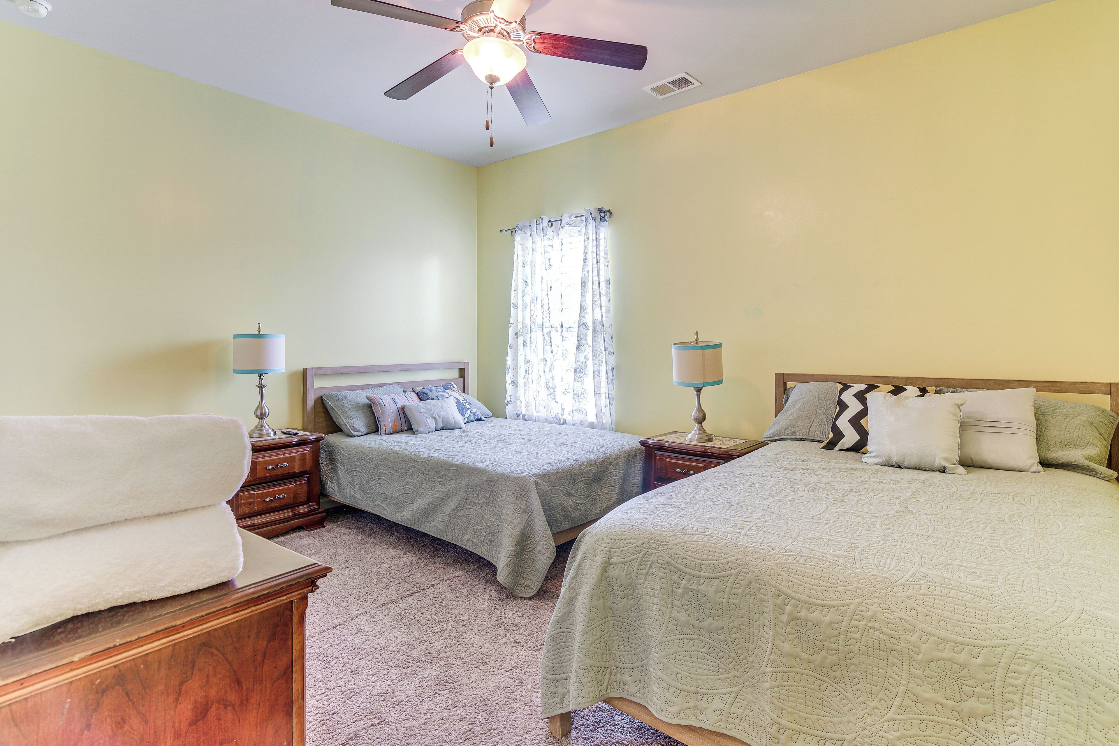 A bedroom with two beds, a ceiling fan, and a window with curtains.