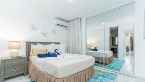 Hotellihuone, jossa on suuri sänky, yöpöytä, peili ja kylpyhuone, joka näkyy lasiovesta.