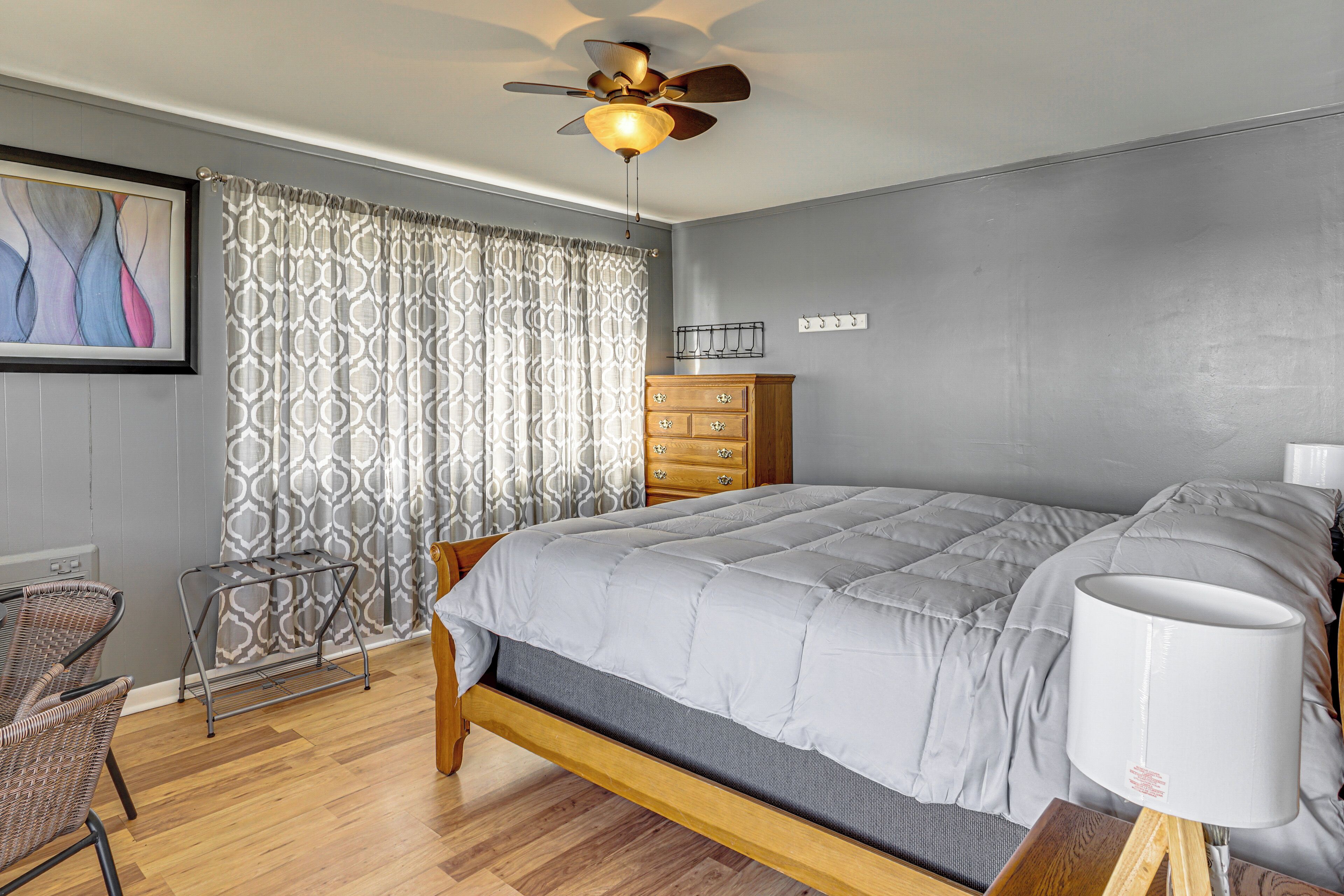 A bedroom with a bed, a dresser, a chair, a ceiling fan, and a wall-mounted light fixture.