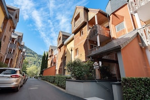 A row of multi-story wooden buildings with balconies, a clear sky, and a car parked on the street. - L'Izard, Pool and Spa, Parking (Cauterets)