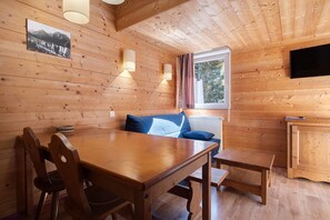 A wooden cabin interior with a dining table, chairs, a sofa, a television, and a window with curtains. - L'Izard, Pool and Spa, Parking (Cauterets)