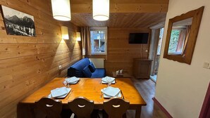 A wooden interior with a dining table set for four, a blue sofa, and a television mounted on the wall. - L'Izard, Pool & Spa, Parking (Cauterets)