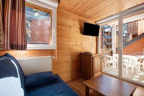 A wooden cabin interior with a sofa, a TV mounted on the wall, and a sliding glass door leading to an outdoor seating area. - L'Izard, Pool and Spa, Parking (Cauterets)