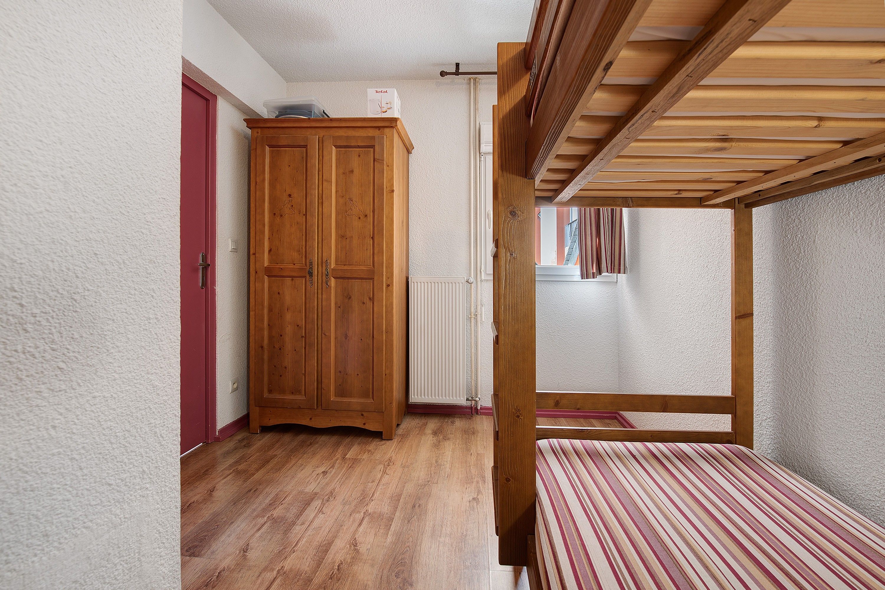 A room with a wooden wardrobe, a radiator, and a window with curtains.