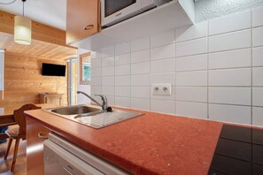 Cozinha com bancada vermelha, pia de aço inoxidável e painel de azulejos brancos.