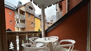 A balcony with white plastic chairs and a table, overlooking a row of colorful buildings with balconies. - L'Izard, Pool & Spa, Parking (Cauterets)