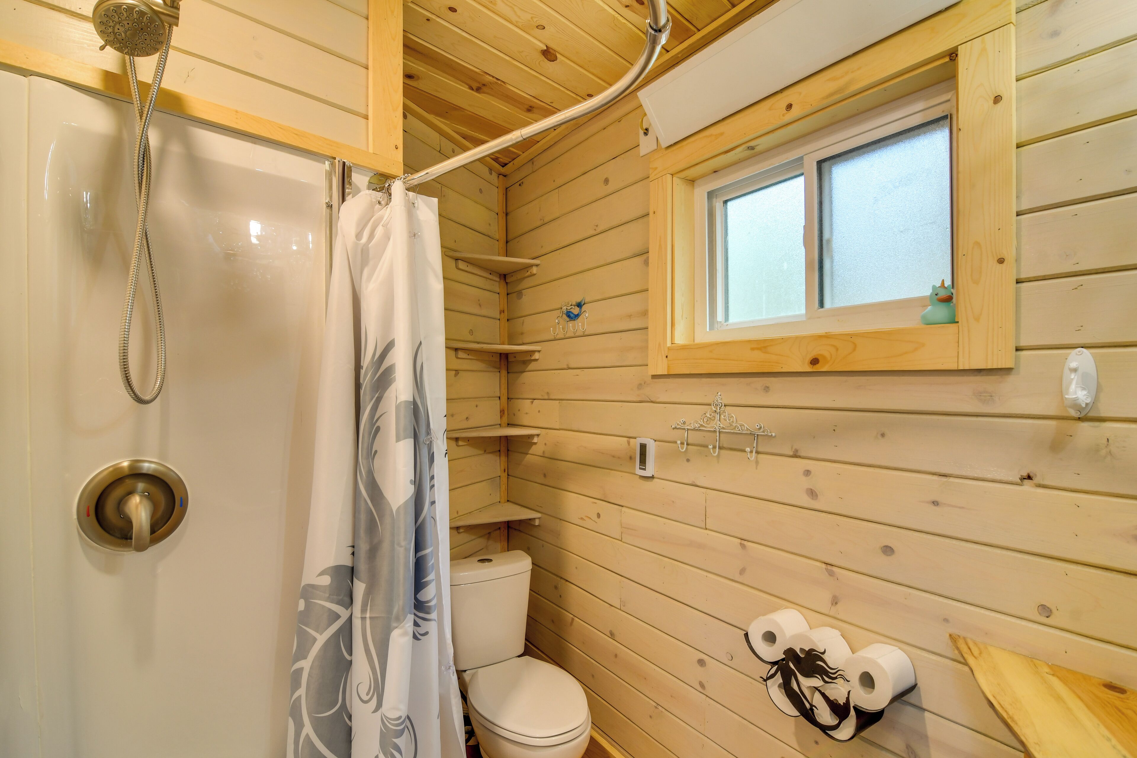 A wooden cabin bathroom with a shower, toilet, and window.